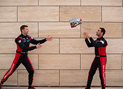2 men in racing suits throwing a Mobil 1 bottle to each other